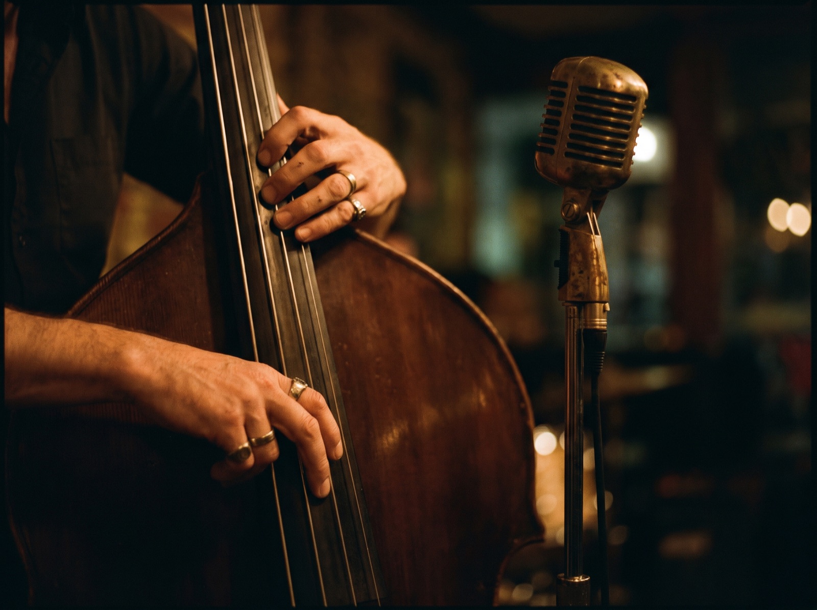 Hands on an upright bass next to a vintage microphone, in warm light